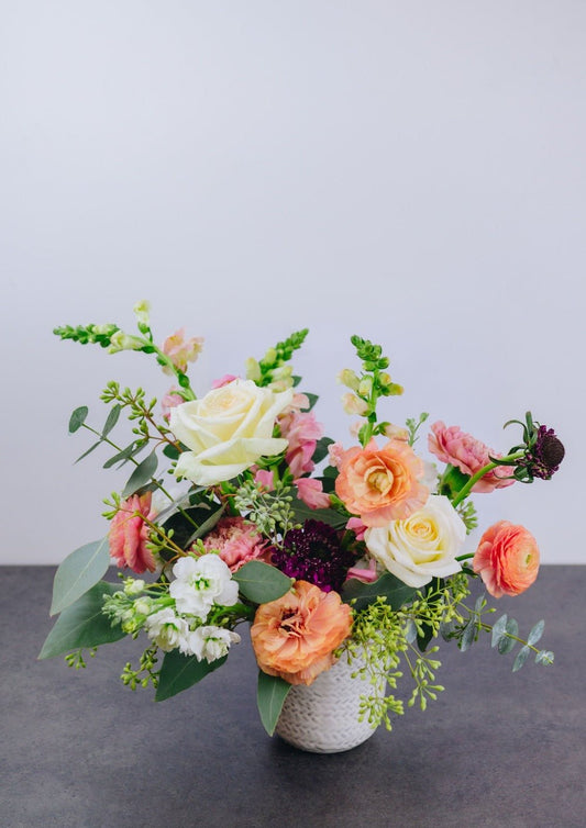 Small bouquet of white, peach, pink, and white flowers with greenery like eucalyptus.