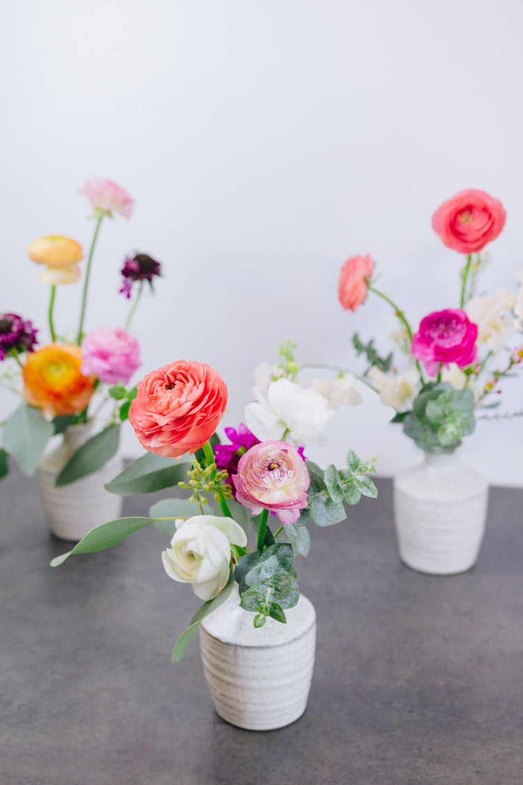 Three white bud vases holding bright springy floral bouquets.