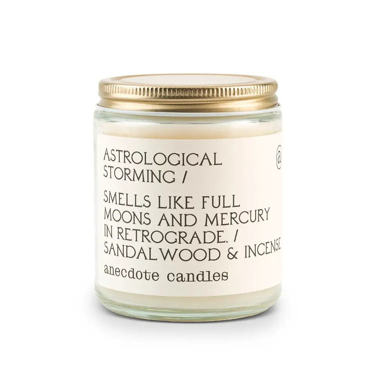 White Anecdote brand candle with label reading Astrological storming / Smells like full moons and mercury in retrograde. / Sandal wood & incense.