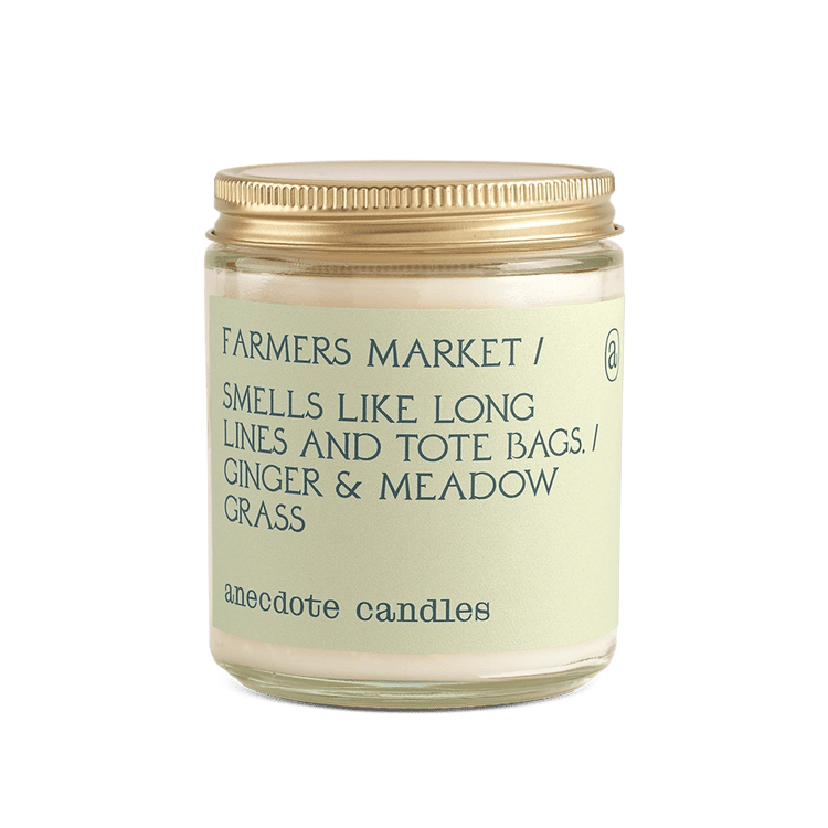 White Anecdote candle with label reading Farmers Market / Smells like long lines and tote bags. / Ginger and meadow grass.