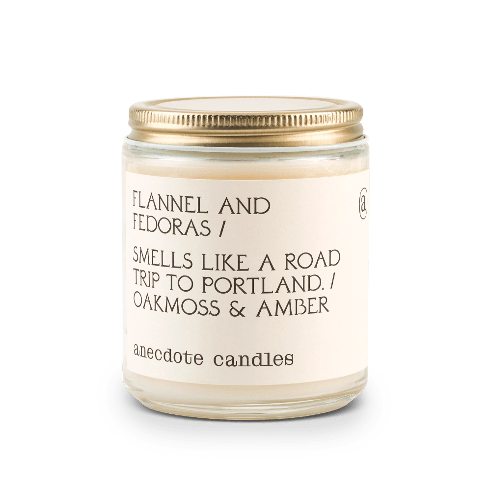 White Anecdote candle with label reading Flannel and Fedoras / Smells like a road trip to Portland. / Oakmoss & amber