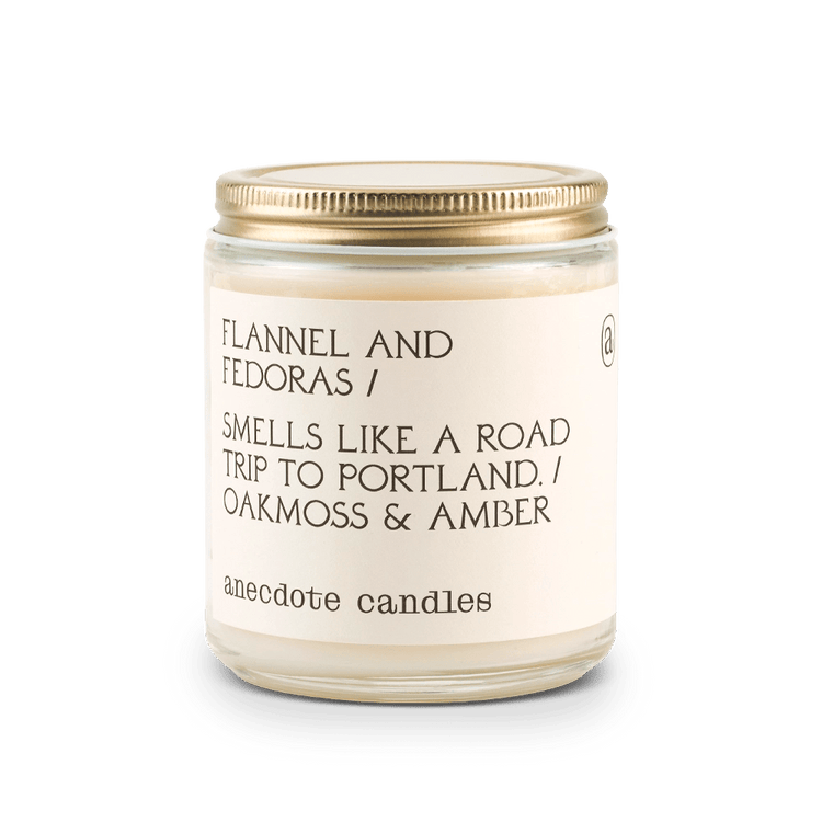 White Anecdote candle with label reading Flannel and Fedoras / Smells like a road trip to Portland. / Oakmoss & amber