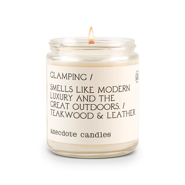 White Anecdote candle with label reading Glamping / Smells like modern luxury and the great outdoors. / Teakwood & Leather