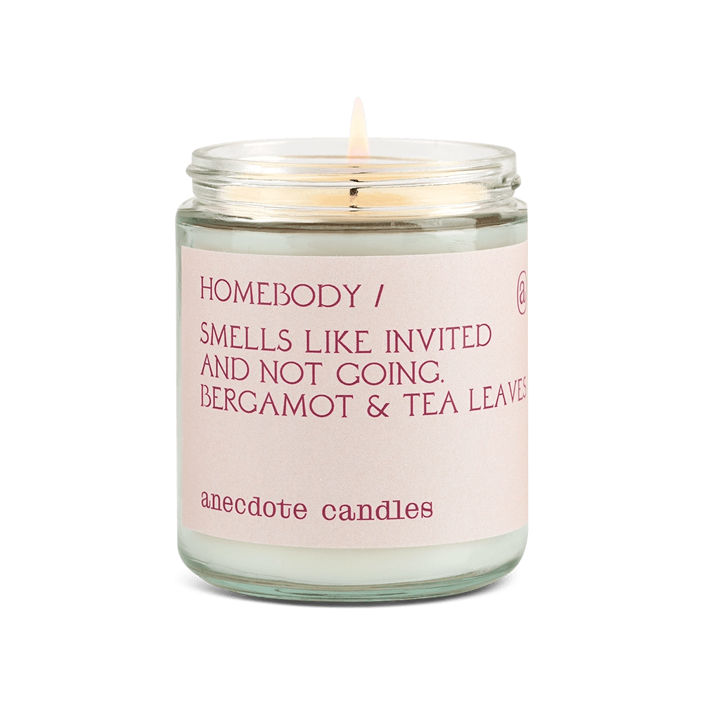 Anecdote candle with pink label reading Homebody / Smells like invited and note going. Bergamot and tea leaves.