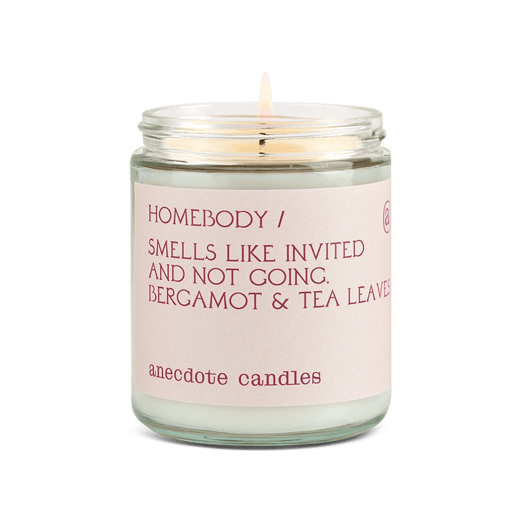 Anecdote candle with pink label reading Homebody / Smells like invited and note going. Bergamot and tea leaves.