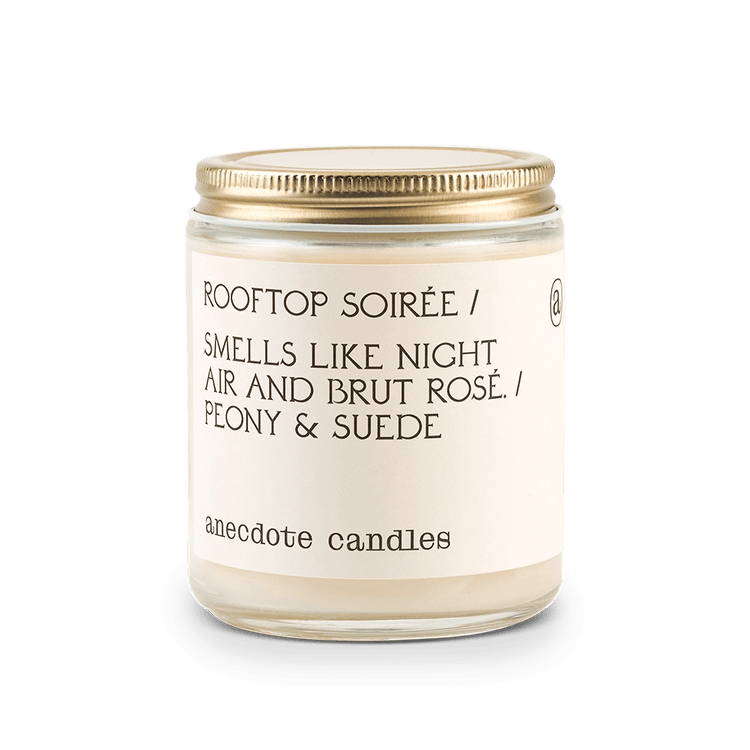Candle with label that reads Rooftop Soiree / Smells like night air and brut rose. / Peony and suede.