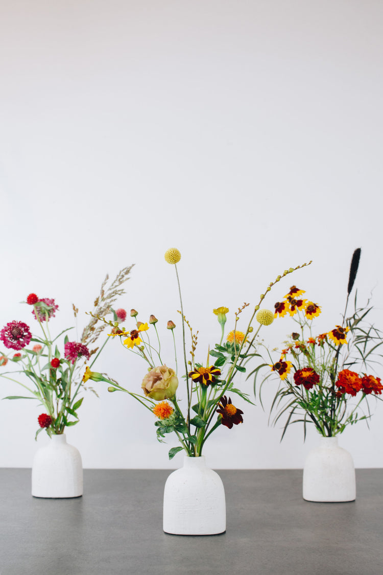 Three seasonal bud vases holding small floral arrangements.