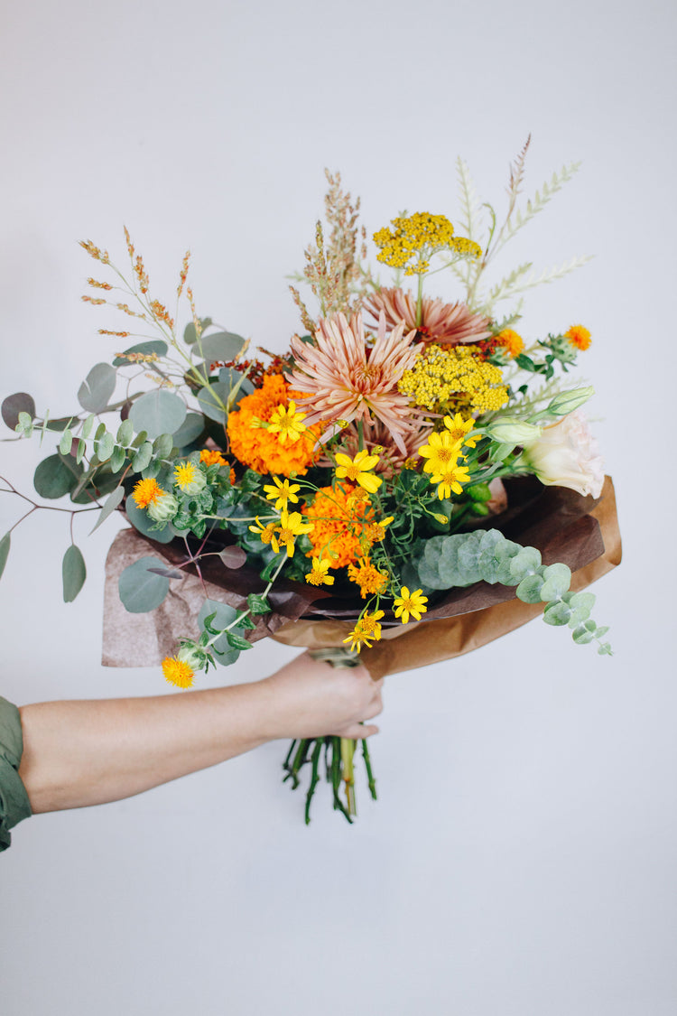 Hand holding bright yellow floral bouquet in paper wrapping.